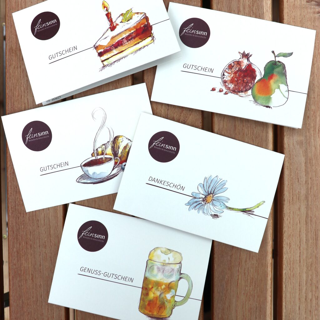 Unterschiedliche Gutscheinmotive liegen auf einem Holztisch