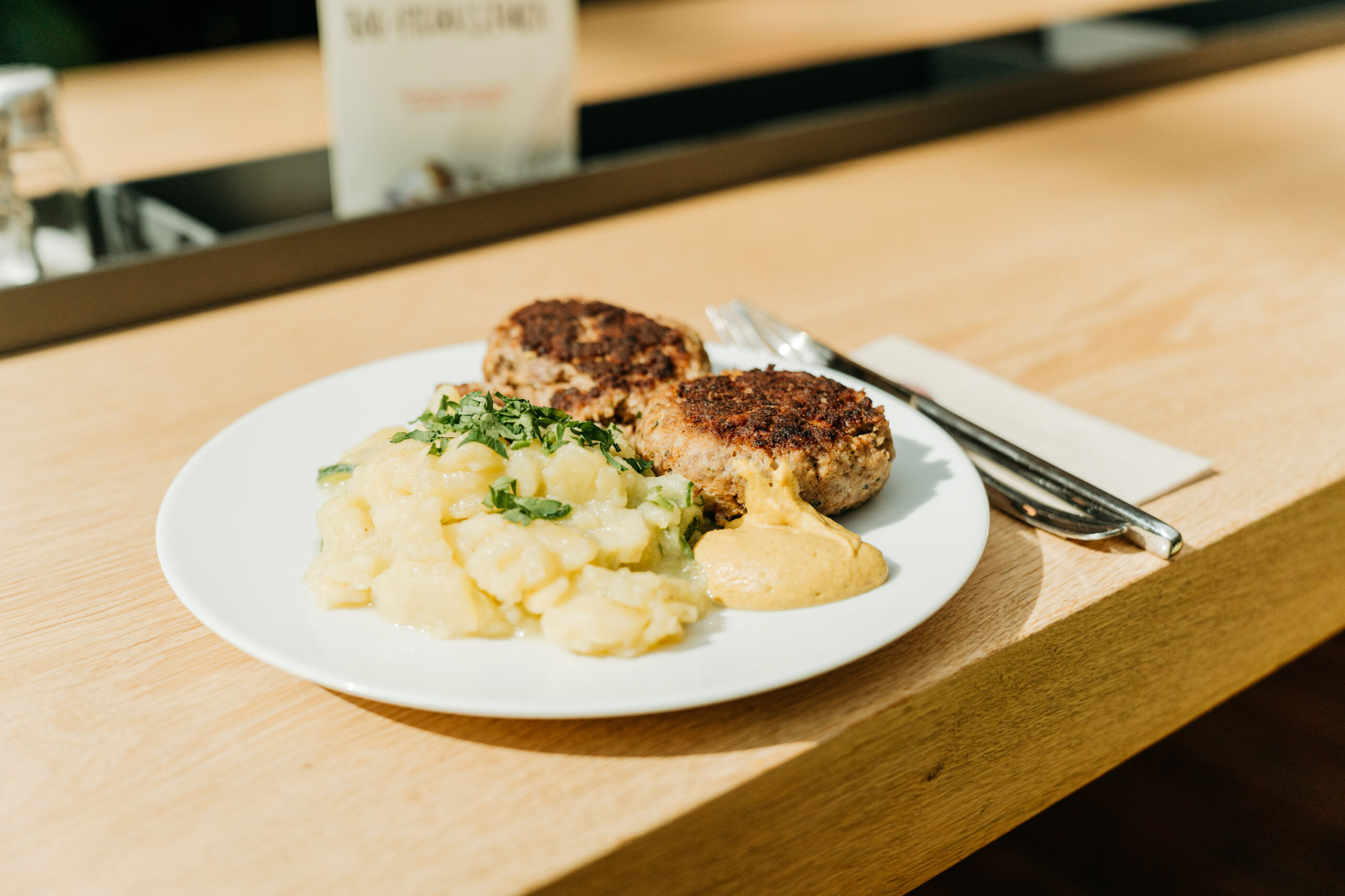 Fleischpflanzerl mit Senf und Kartoffelsalat angerichtet auf Teller, mit Besteck und Serviette